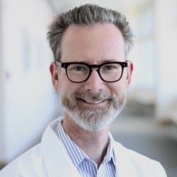 Professional smiling man in glasses, representing consciousness and healing with psychedelic medicin.